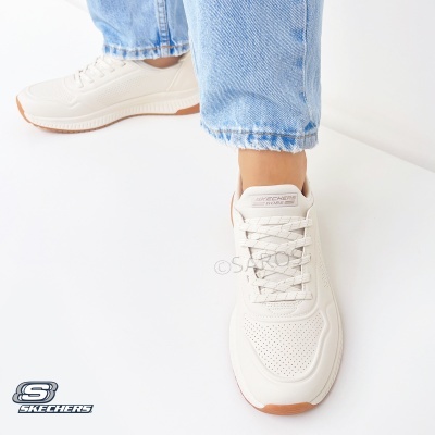 Ténis Skechers brancos com sola castanha usados com calças de ganga azuis