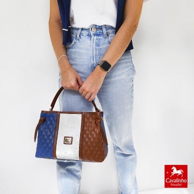 Mala acolchoada azul, branca e castanha com logótipo Cavalinho, mulher com jeans e t-shirt a segurá-la