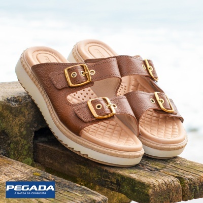 Sandálias castanhas de dedo com fivelas douradas sobre madeira à beira da água