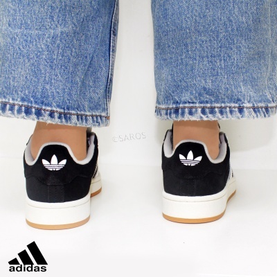 Ténis Adidas pretos com sola branca e logotipo na parte traseira, usados com jeans azuis.