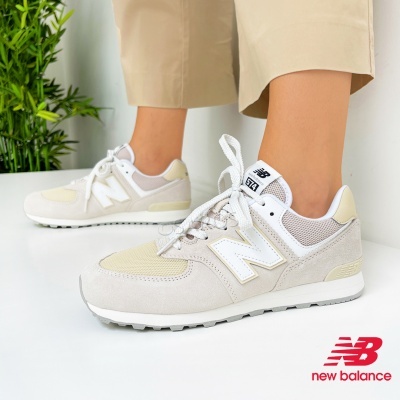 Sapatilhas New Balance 574 creme e branco usadas por pessoa, com planta verde e fundo branco