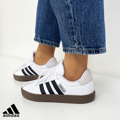 Ténis Adidas brancos com riscas pretas usados com calças de ganga azuis