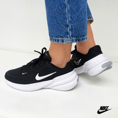 Tênis desportivos Nike pretos com sola branca usados com jeans azuis