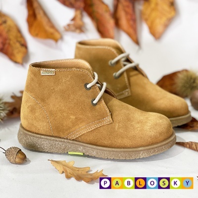 Botas castanhas de criança em camurça com atacadores cinzentos e sola de borracha sobre fundo branco com folhas secas