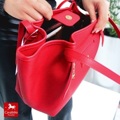 Mala feminina vermelha aberta com fecho dourado e alças manuseada por mãos
