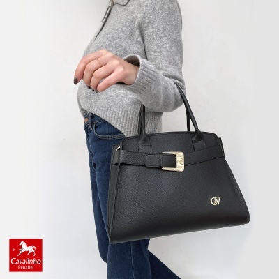 Mala de senhora preta em pele com fivela dourada e logótipo CV, vista ao ombro com mulher de camisola cinza e jeans