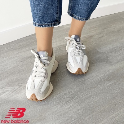 Ténis New Balance brancos e cinzentos usados, chão de madeira cinzenta