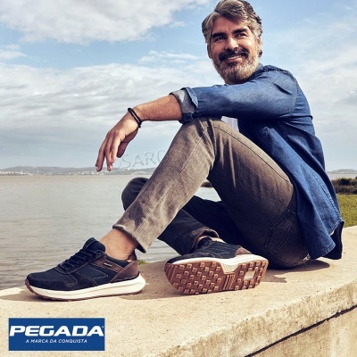 Homem sentado à beira-mar com sapatilhas pretas da marca PEGADA.