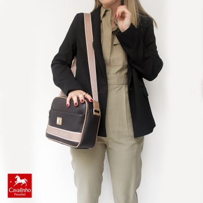 Pessoa com mala tiracolo preta e bege Cavalinho, blazer preto e macacão bege