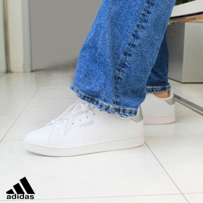 Sapatilhas brancas Adidas Stan Smith com detalhes cinzentos usadas com calças de ganga azuis