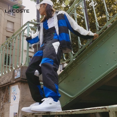 Pessoa com fato de treino multicolorido e sapatilhas brancas junto a estrutura metálica verde