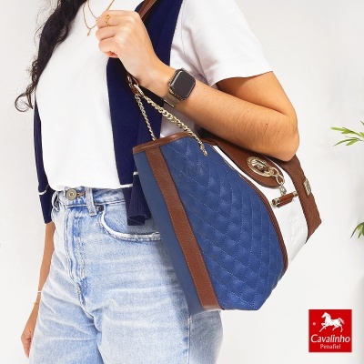 Mala Cavalinho azul, branco e castanho com detalhes dourados ao ombro de mulher