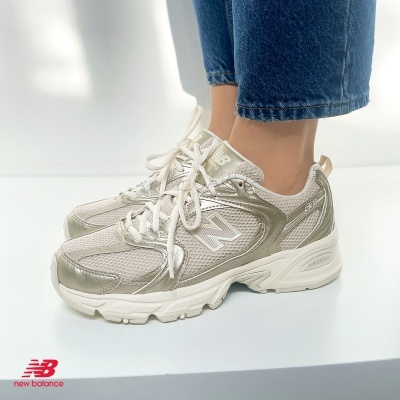 Ténis New Balance 530 brancos e prateados usados com jeans azuis