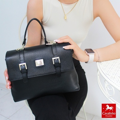 Mala de mão preta em pele texturada com fivelas douradas e mulher segurando