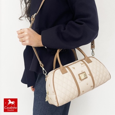 Mala bege e castanha Cavalinho Penafiel com padrão acolchoado e logótipo em metal, usada ao ombro por pessoa com casaco preto.