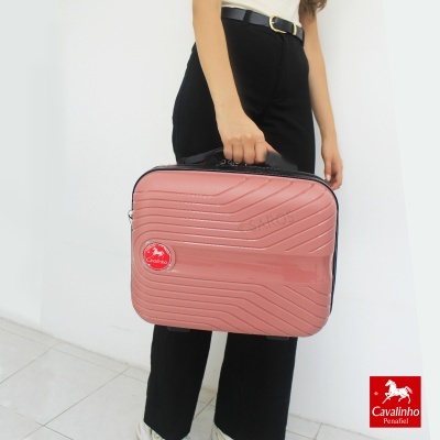 Mala de viagem rosa claro com etiqueta Cavalinho, segurada por pessoa com calças pretas