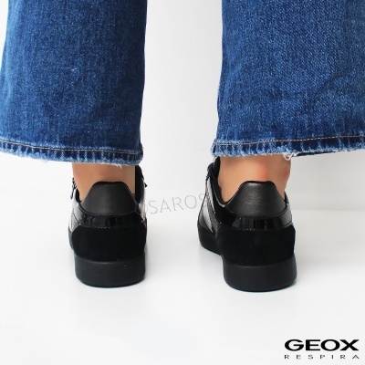 Sapatilhas pretas vistas de trás com jeans azuis em fundo branco