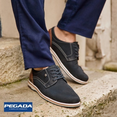 Sapatos masculinos pretos com sola branca e detalhe castanho usados com calças azuis em degraus de pedra