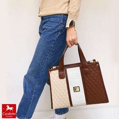 Mala de mão matelassê castanha, branca e bege segurada por pessoa com jeans azul e camisola bege