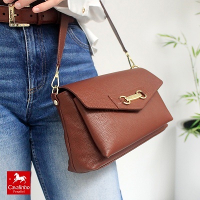 Mala castanha de couro com fecho dourado e alça ajustável usada com jeans e cinto castanho