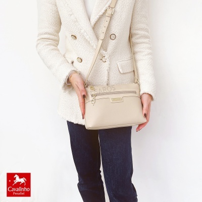 Mala de tiracolo bege com casaco creme e calças escuras.