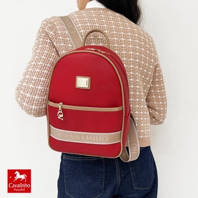 Mochila vermelha com detalhes em bege e alças Cavalinho numa mulher com casaco bege e jeans.