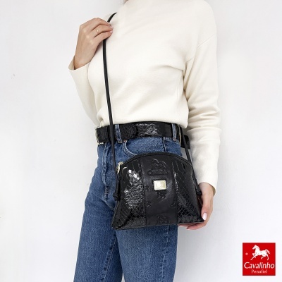 Bolsa preta pequena em pele croco com alça fina mostrada numa modelo com camisola branca e jeans