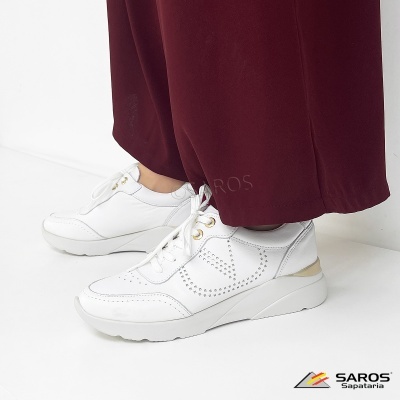 Ténis brancos com detalhes perfurados e atacadores com ilhós dourados junto a calças vermelhas