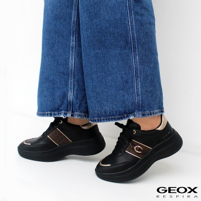 Ténis Geox pretos com detalhes castanhos e dourados junto a calças de ganga azuis