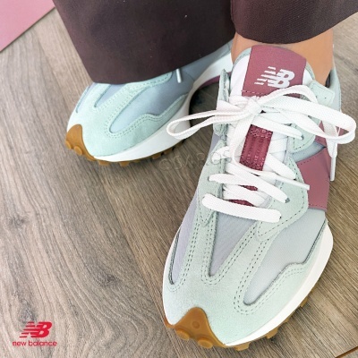 Ténis New Balance verde-água e bordeaux com atacadores brancos num chão de parquet.