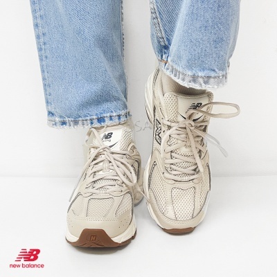 Ténis de corrida New Balance bege com detalhes em malha usados com jeans azuis em fundo branco