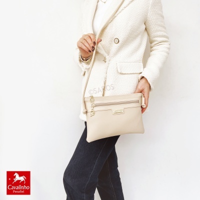 Mulher com casaco branco e mala bege tiracolo contra fundo branco