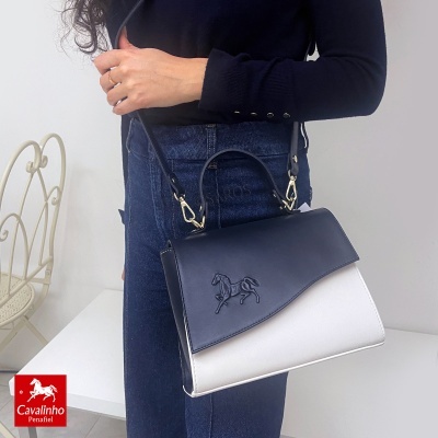 Mala Cavalinho azul escuro e branco com relevo de cavalo, mostrada ao ombro