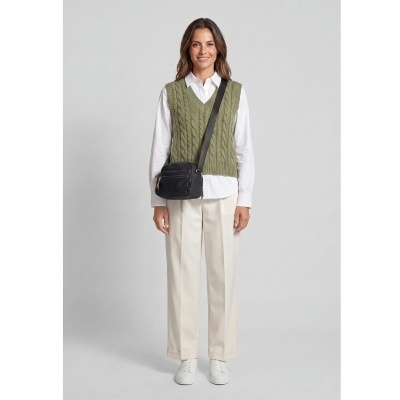 Mulher com camisa branca, colete verde, calças creme, sapatilhas brancas e bolsa preta tiracolo