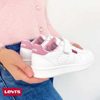 Ténis brancos LEVI'S com detalhes rosa e etiqueta vermelha junto a mãos segurando-os