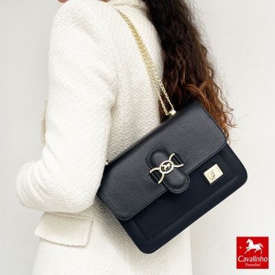 Bolsa preta de couro com fecho dourado e alça de corrente usada com casaco branco