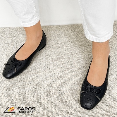 Sapatos rasos pretos perfurados com laço frontal em mulher com calças brancas