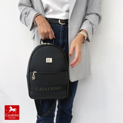 Mochila preta Cavalinho com fecho dourado e logótipo, segurada por pessoa.