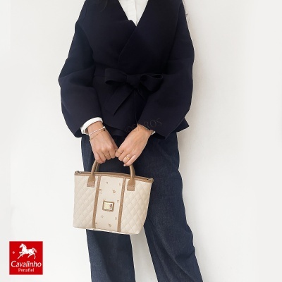Mala de mão bege e castanho Cavalinho Penafiel com padrão e matelassê. Acessório feminino em ambiente neutro