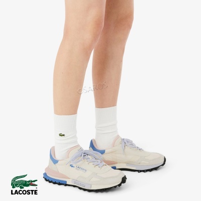 Sapatilhas creme, rosa e azul Lacoste com meias brancas de logótipo verde em pernas femininas