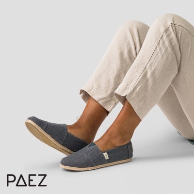 Alpargatas cinzentas Paez com sola beje em modelo sentado, calças bege clara.