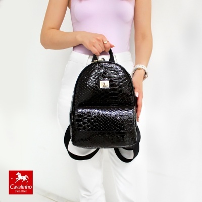 Mochila preta com textura brilhante tipo pele de crocodilo segurada à frente por pessoa