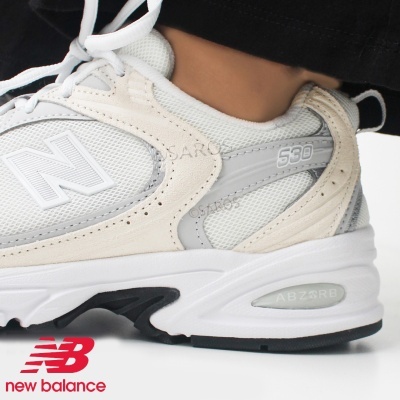 Tênis desportivo New Balance branco, bege e cinza com sola branca e preta.