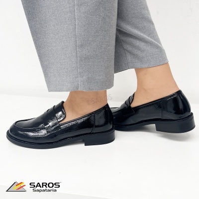 Sapatos mocassin pretos em pele verniz com sola preta e calças cinzentas.