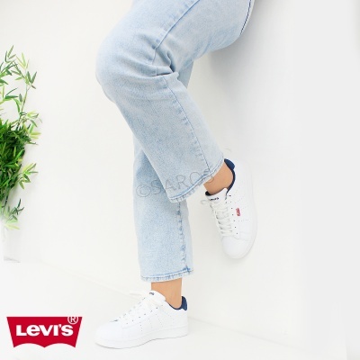 Ténis brancos Levi's com detalhes azul escuro usados por pessoa com calças de ganga claras