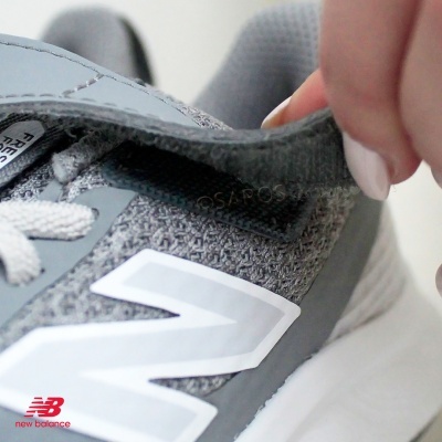 Ténis New Balance cinzento com logótipo branco e sola branca, visto de perto com detalhe da aba interior segurada