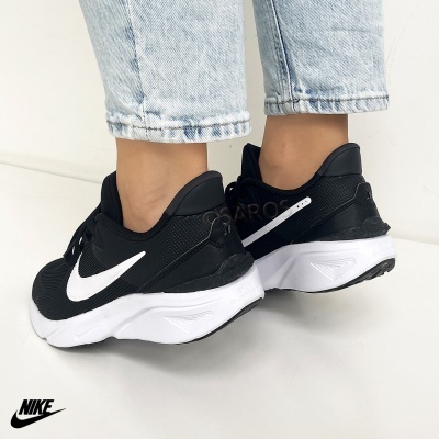 Ténis Nike pretos com logo branco e sola branca usados com calças de ganga claras.