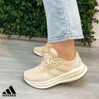 Ténis Adidas bege com sola branca em piso cinza e fundo decorado com plantas verdes