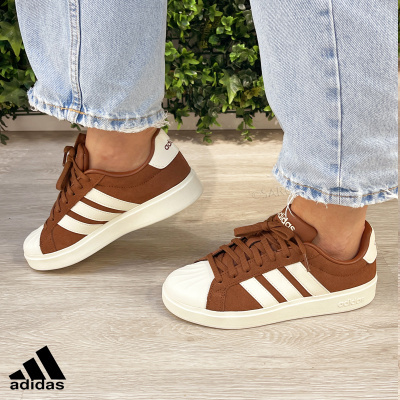 Ténis Adidas castanhos com riscas brancas usados com jeans azuis desfiados