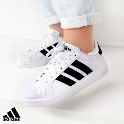 Ténis Adidas brancos com riscas pretas usados com calças de ganga claras.